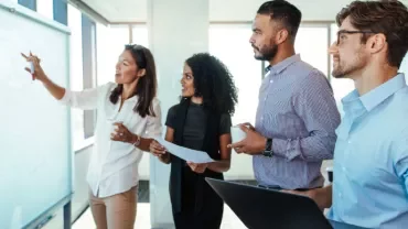 Four colleagues discussing a project at a whiteboard in an office.