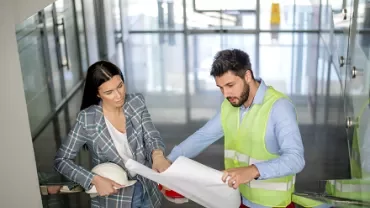 Two people discussing blueprints in a modern office stairwell.