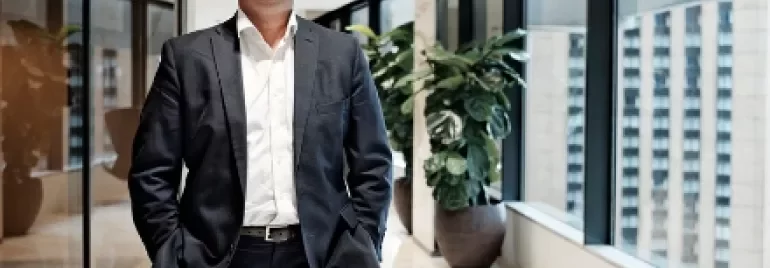 Smiling man in a suit standing in a bright office hallway.
